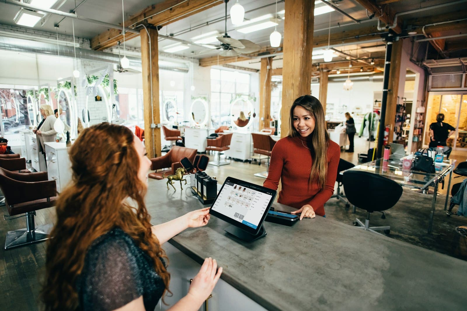 Salon owner smiling with a customer at the front desk of a bright studio