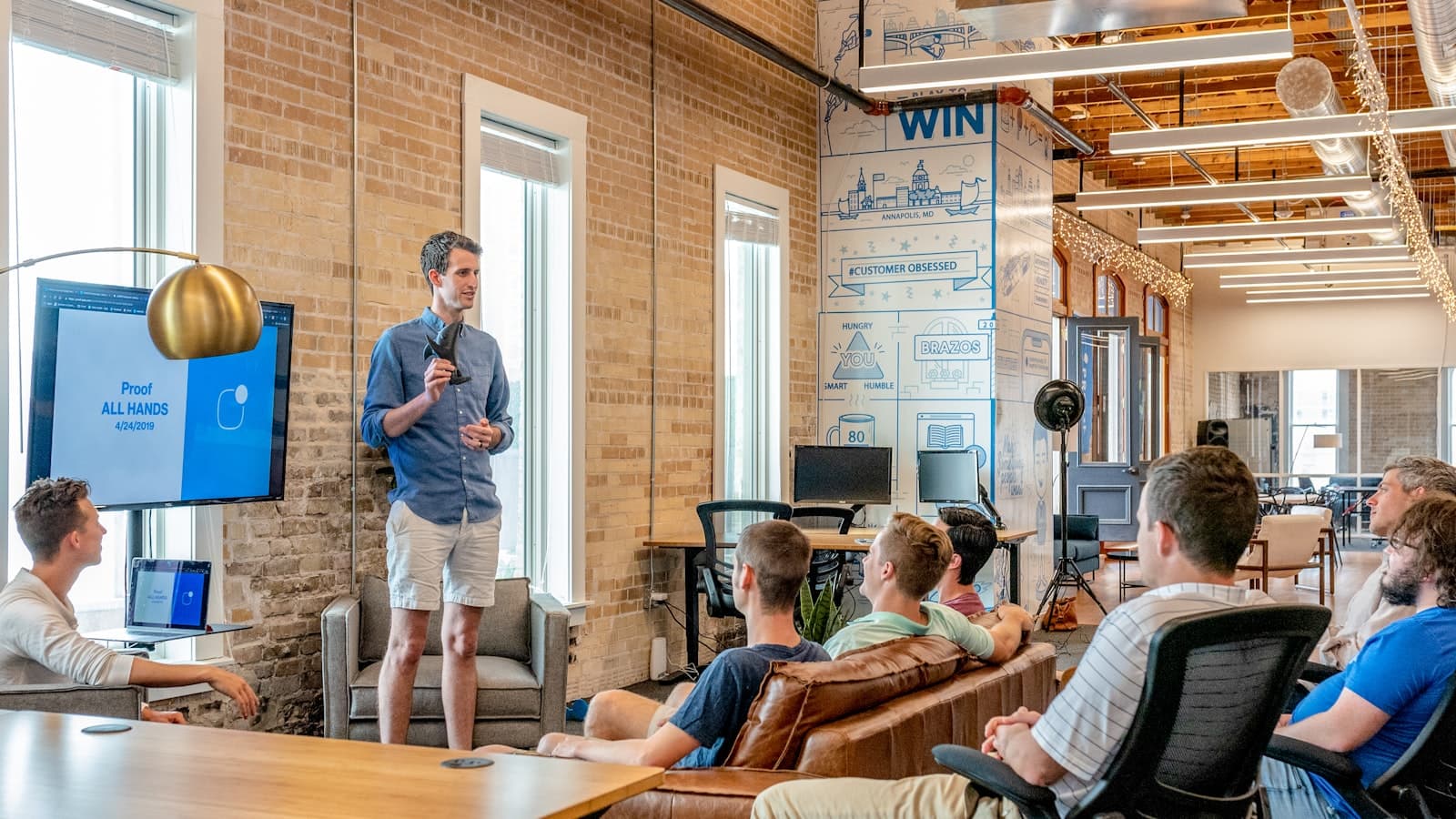 A small team listening to a presentation in a warm brick-walled office