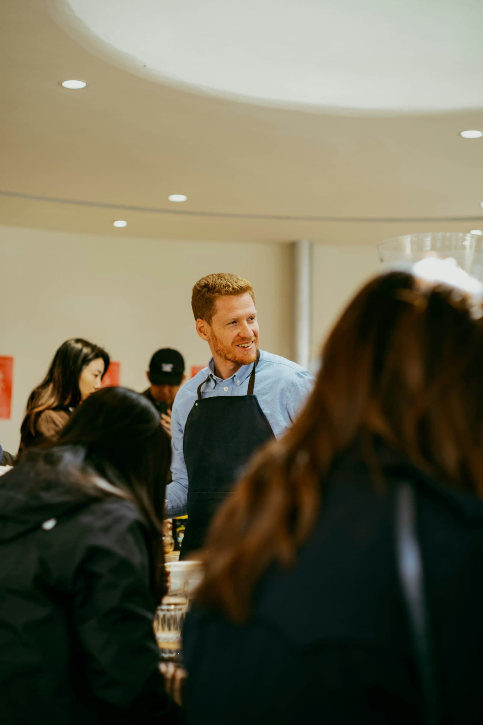 Friendly shop host in an apron welcoming customers in a warm, busy space